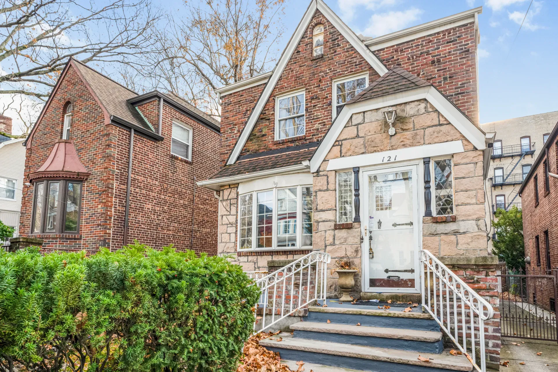 A brick and stone single-family house on a Jersey City street, with a walk-up apartment building adjoining it