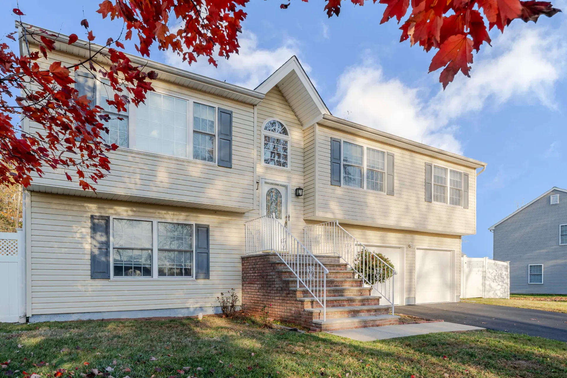 A bi-level house with pale siding in Somerset, New Jersey, framed by a red maple in autumn